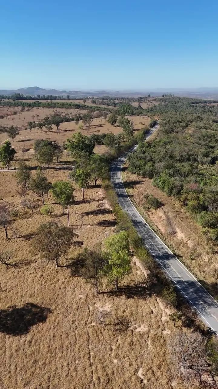 Vista aérea do Planícies da Serra com a estrada asfaltada cortando o terreno e os morros ao fundo
